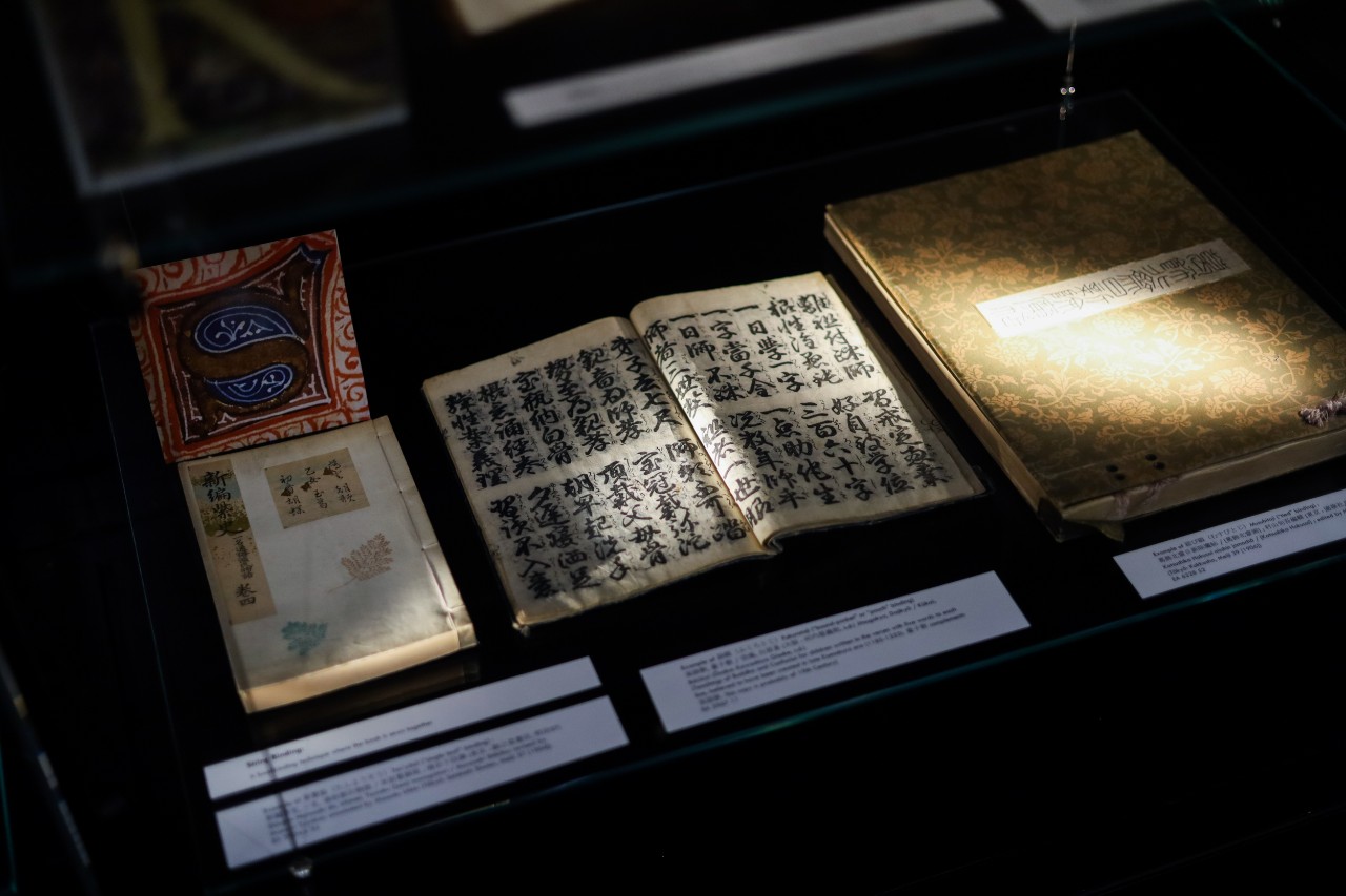 Open books on display in glass cabinets, including a book with Chinese calligraphy