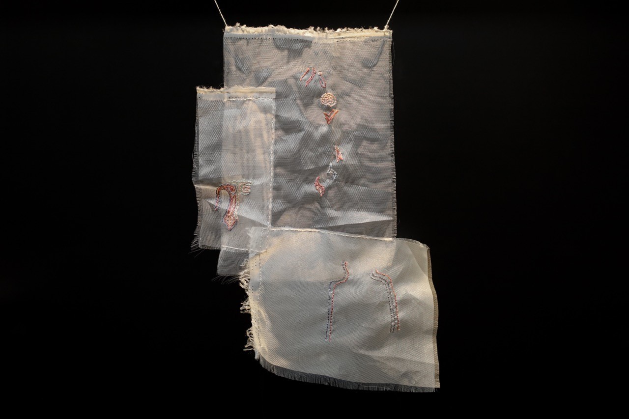 Close up of textile artwork hanging in glass display case