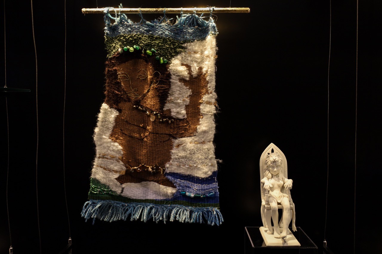 Close up of a woven artwork and small sculpture on display in a glass cabinet