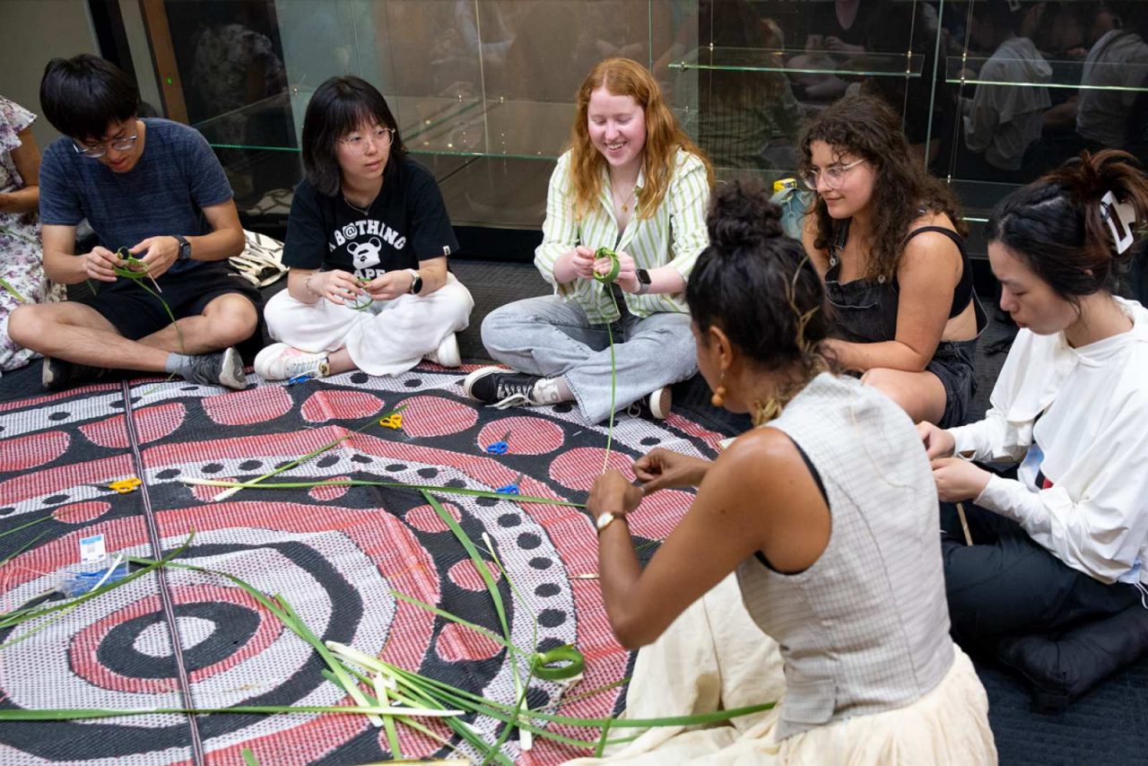 a group of students around a weaving rug