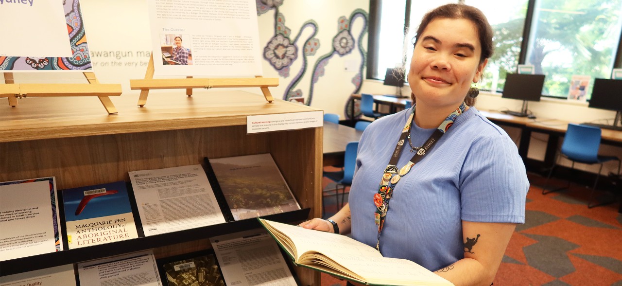 Jamie-lee Ferguson standing beside her NAIDOC Week book display in the Aboriginal and Torres Strait Islanders student space in Fisher Library
