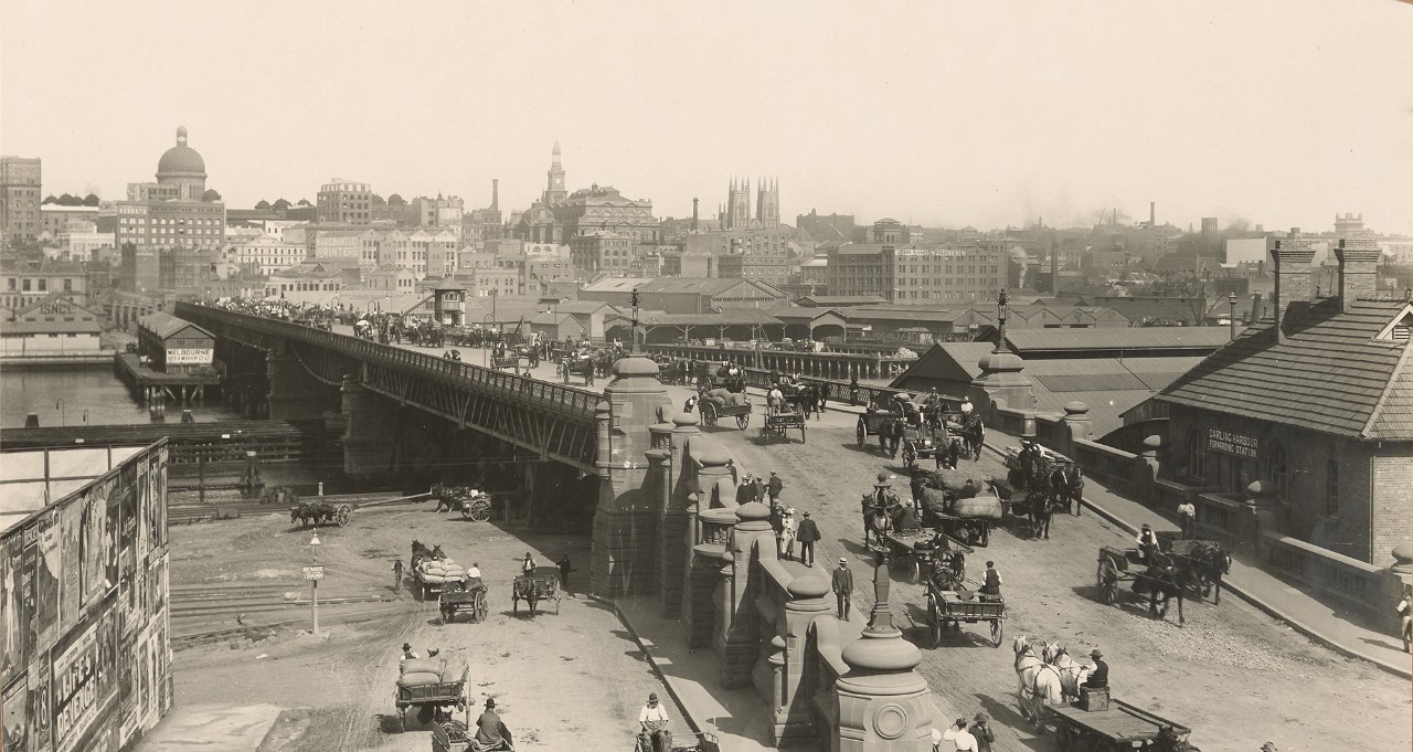 Black and white photo of Pyrmont Bridge between 1890-1930. Crowds of people are on the bridge, as well as horse-drawn carriages. 