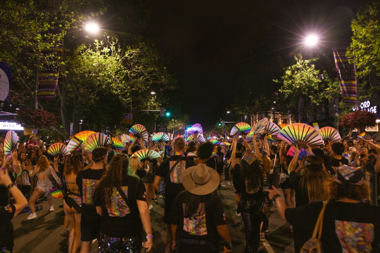 Large crown marching through the streets at night holding fans with the pride progress flag