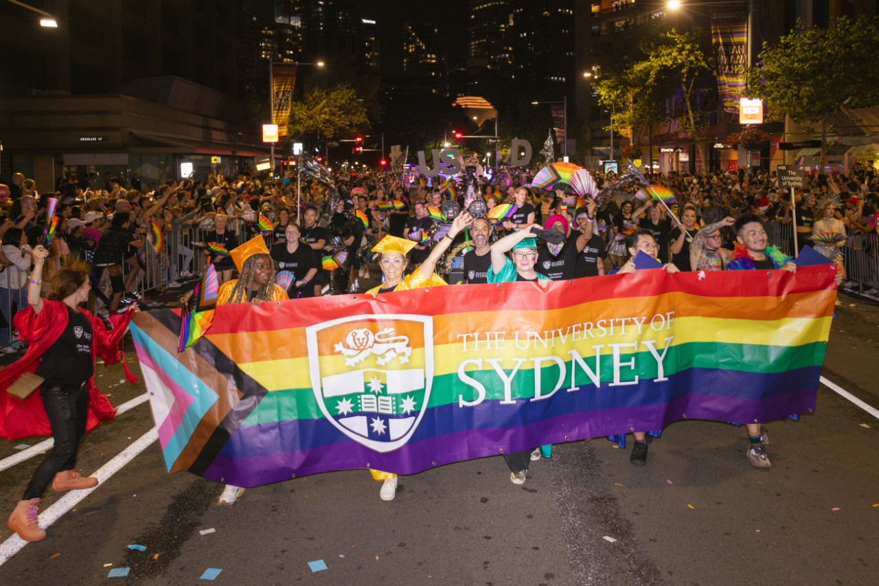 Madri Gras marchers walk down Oxford st behind a rainbow banner with the University of Sydney logo