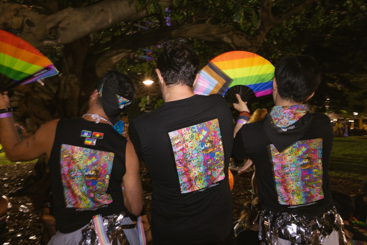 Three people with their backs turned, wearing matching t-shirts with a colourful illustration