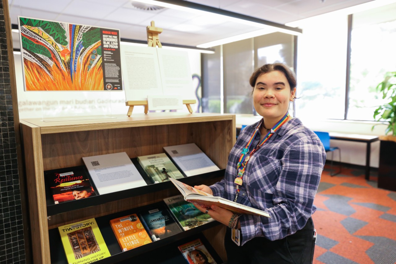 Jamie-lee Ferguson standing beside her NAIDOC Week book display in the Aboriginal and Torres Strait Islanders student space in Fisher Library