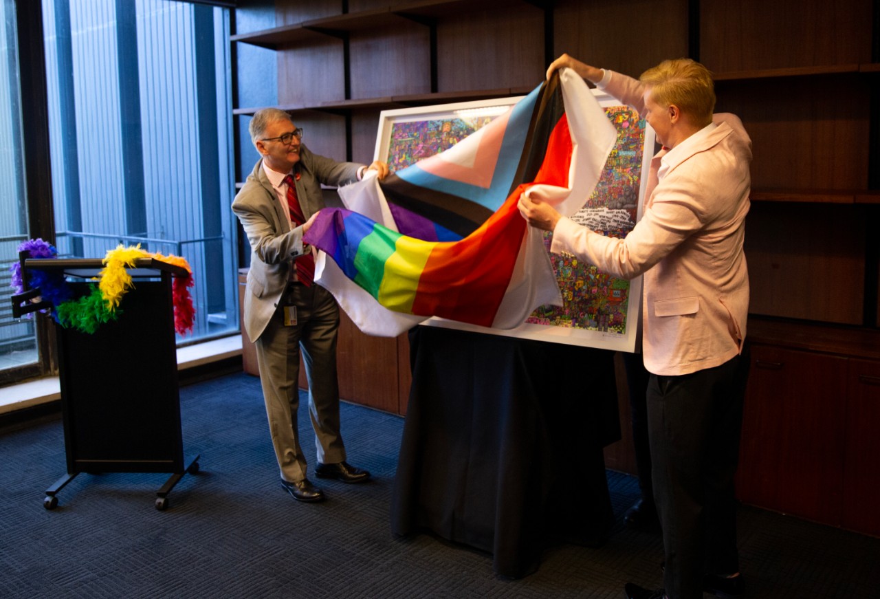 Two people removing a rainbow flag from an artwrok on an easel