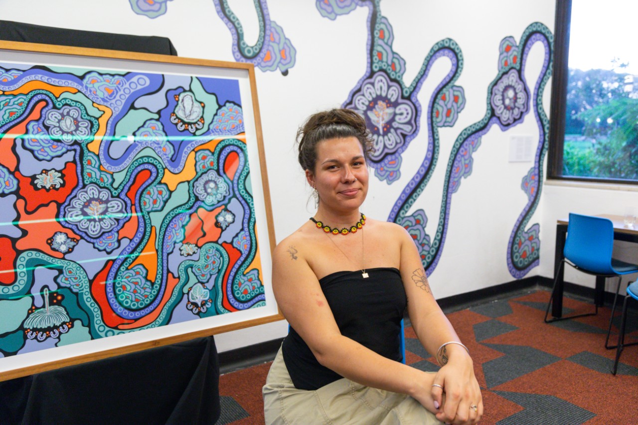 Artist Jessie Waratah seated in front of her artwork 'Walking on Country'
