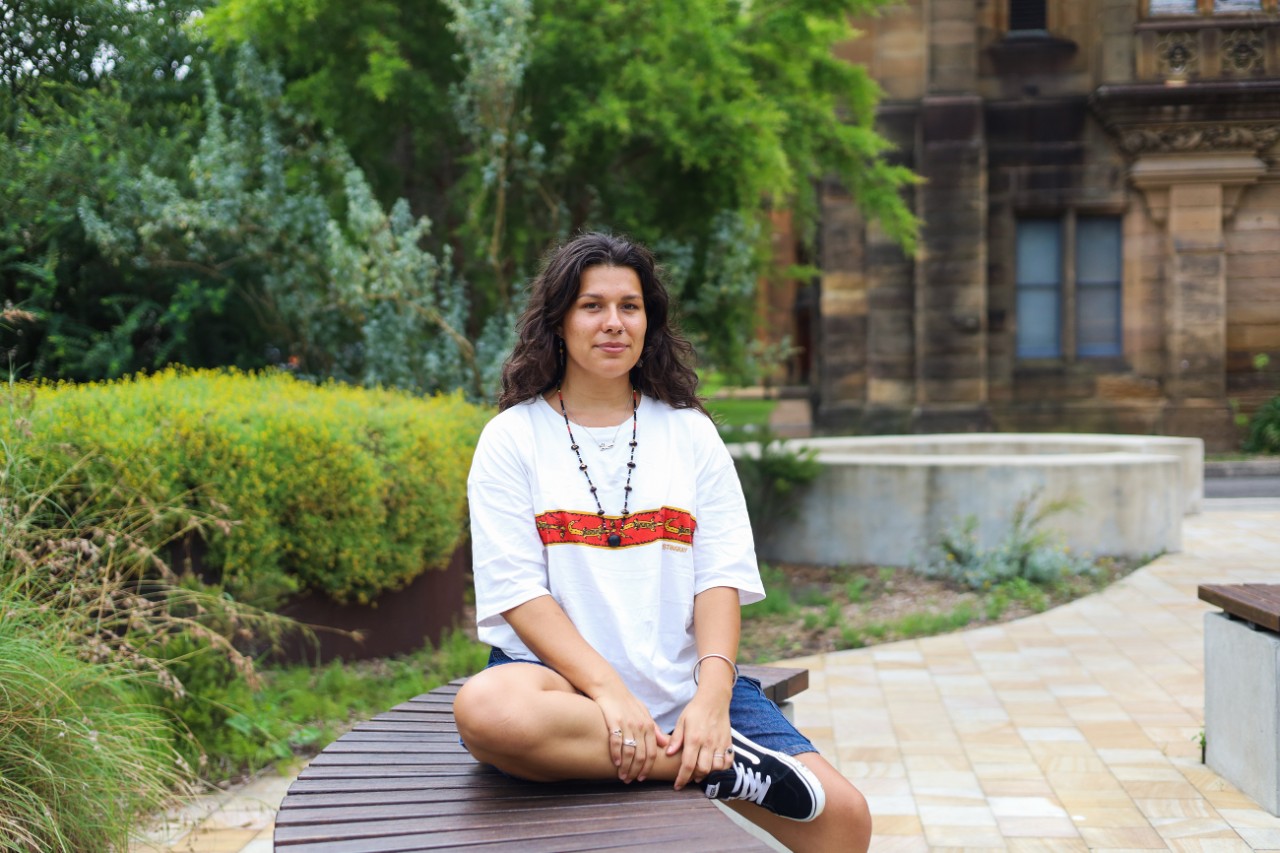 Artist Jessie Waratah sitting on a bench outdoors on the University of Sydney campus