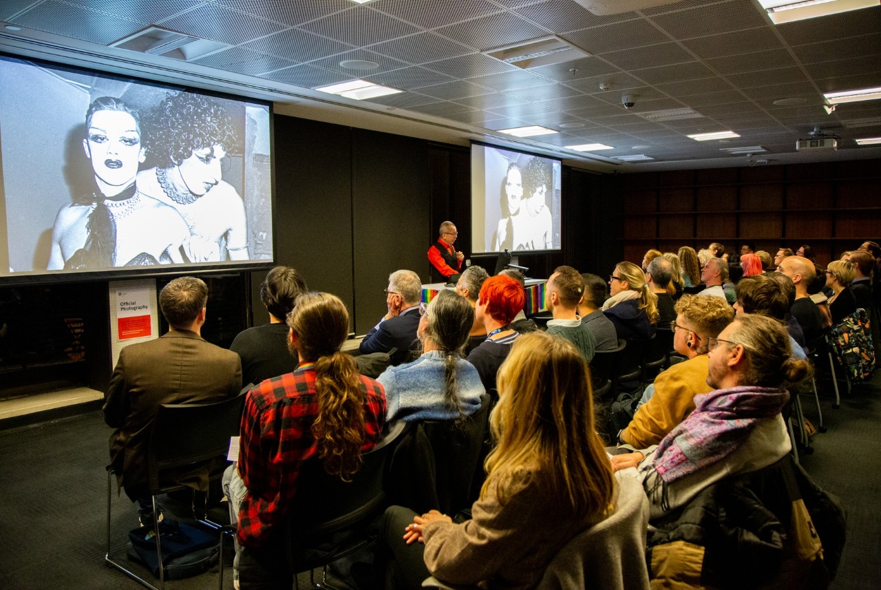 William Yang speaking in front of a large seated audience