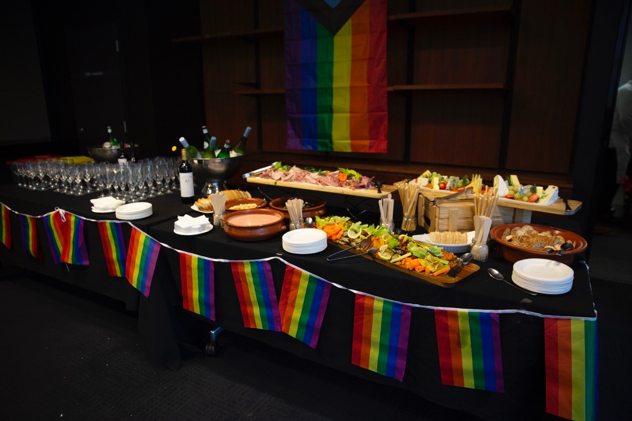 A table of food and drinks, decorated with Pride rainbow flags