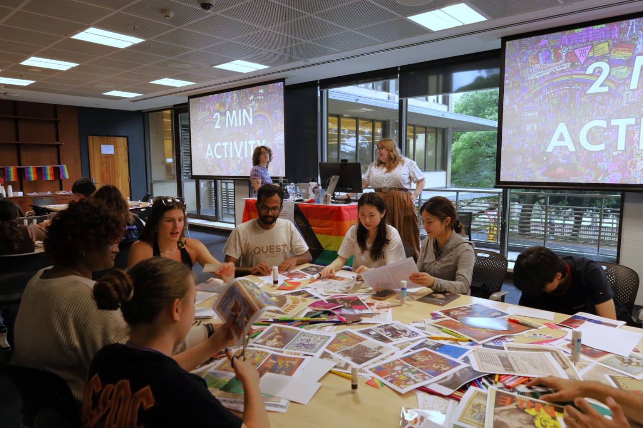 A photograph showing a room full of people sitting around tables strewn with craft materials