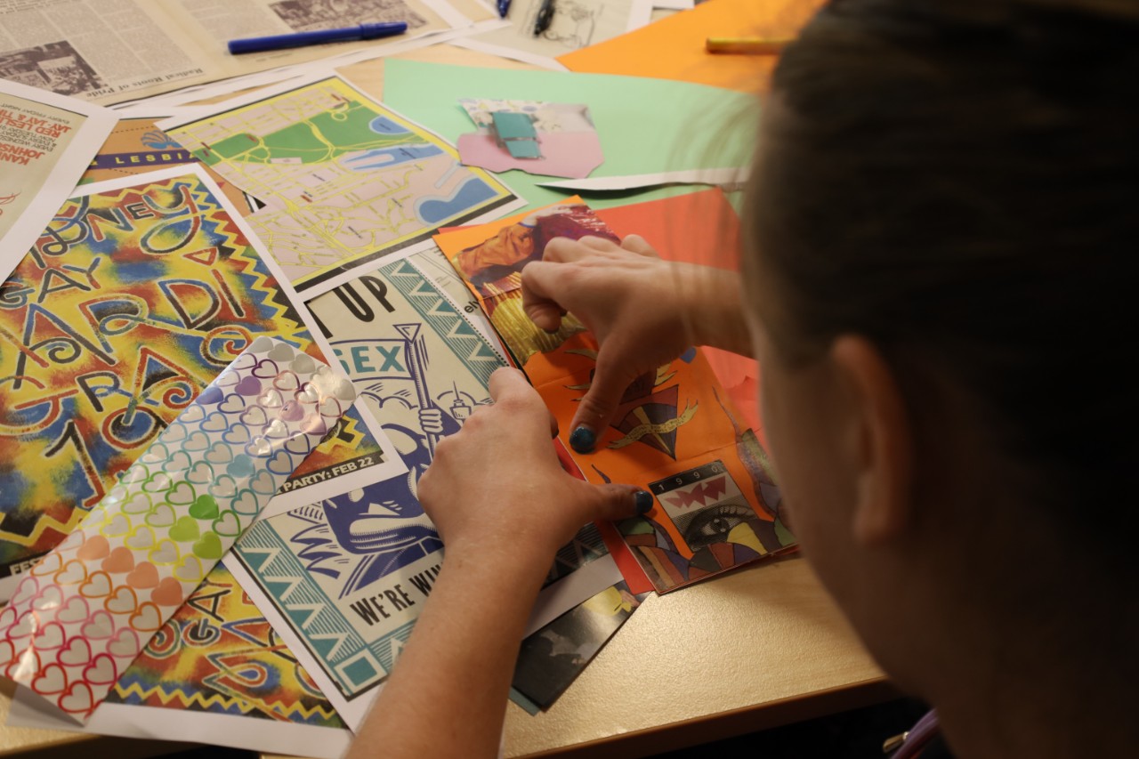 Photo taken over a person's shoulder, showing them working on a zine using materials about the Sydney Gay and Lesbian Mardi Gras