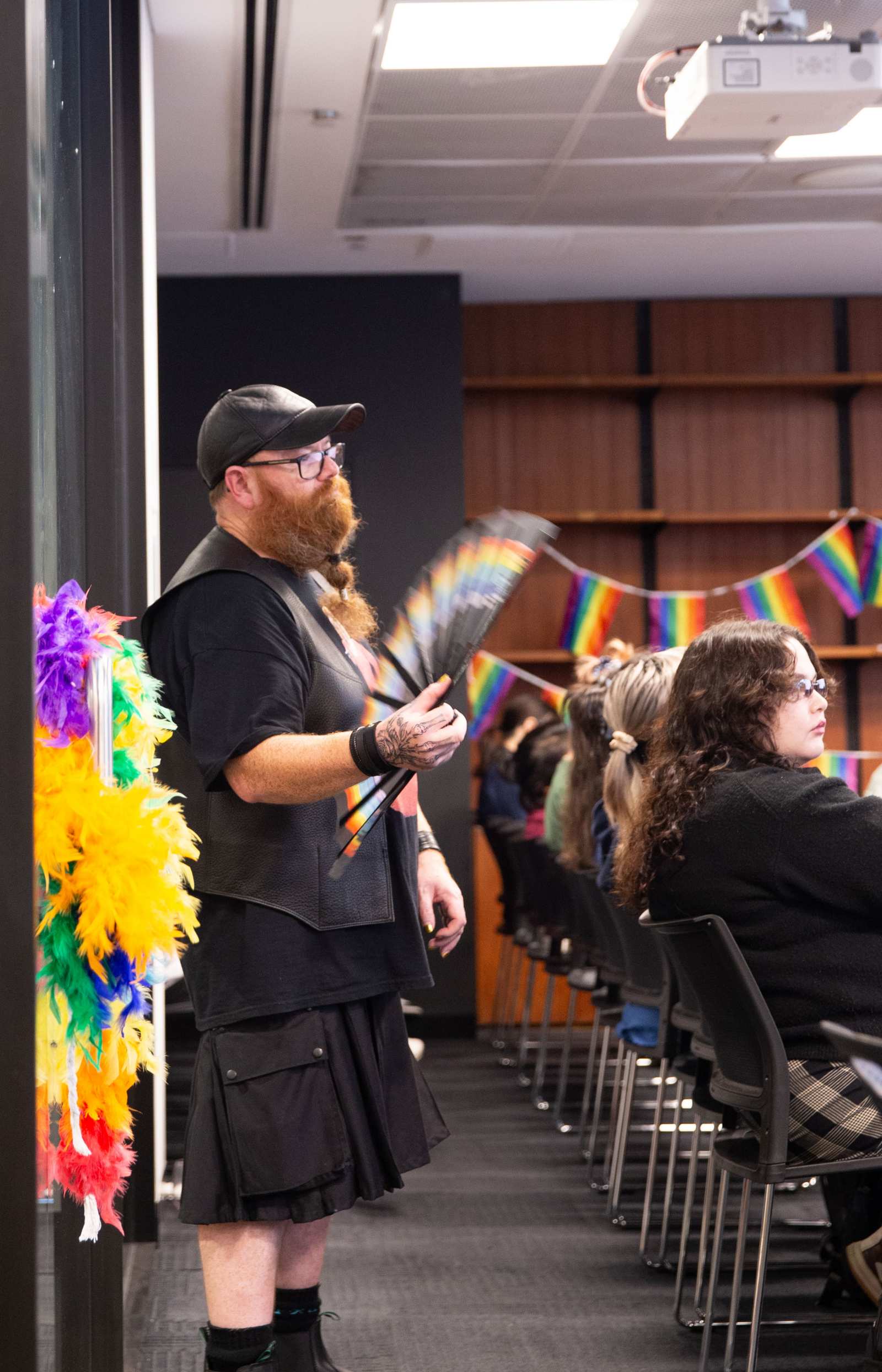 A photograph of Curt Flood (a man with a big red beard wearing an all black outfit), fanning himself with a rainbow fan