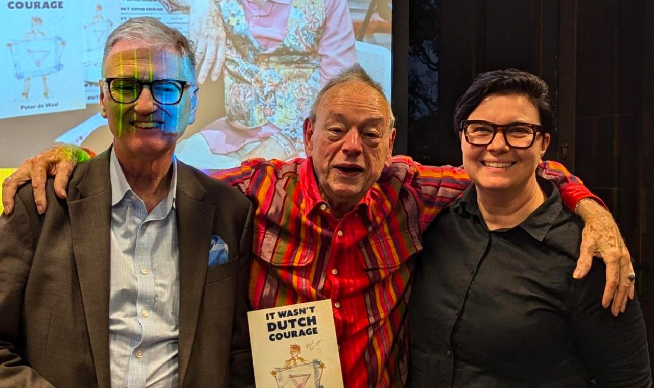 A colour photograph showing three people standing with their arms around each other. On the left is University Librarian Philip Kent (a tall man with glasses and grey hair), in the middle is author and activist Peter de Waal (an elderly man wearing a brightly coloured shirt), and on the right is Director of Operations & Engagement Antonia Mocatta (a woman with short brown hair and glasses)