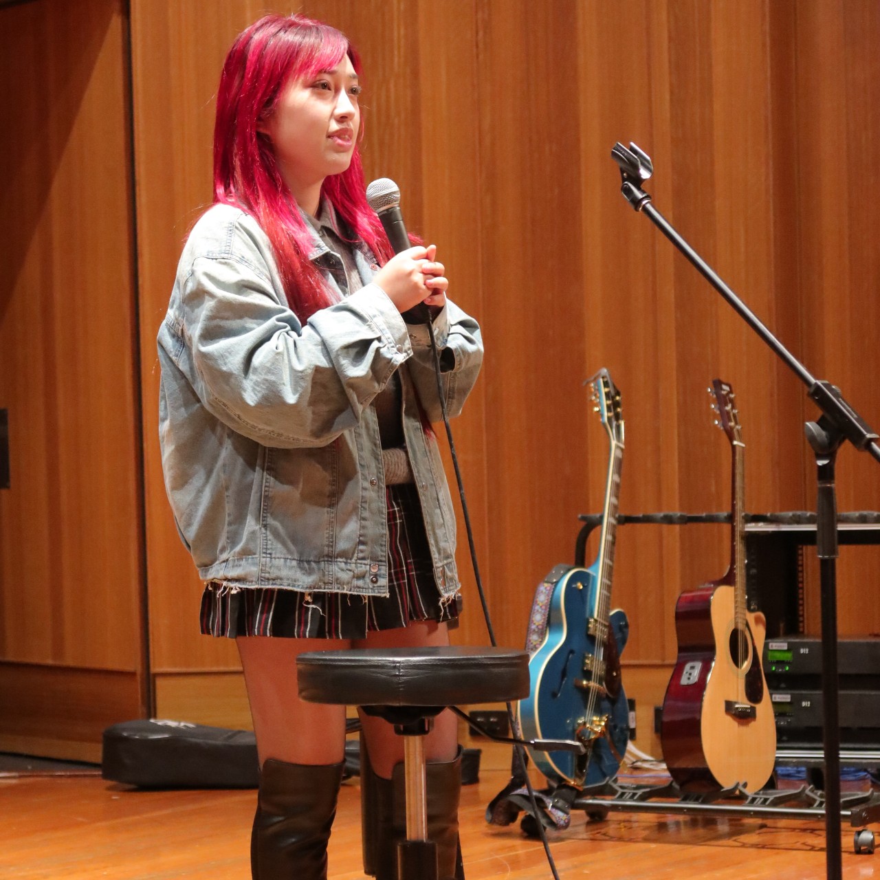 A colour photograph of Yizhen Wang, a young woman with bright pink hair, singing into a microphone.